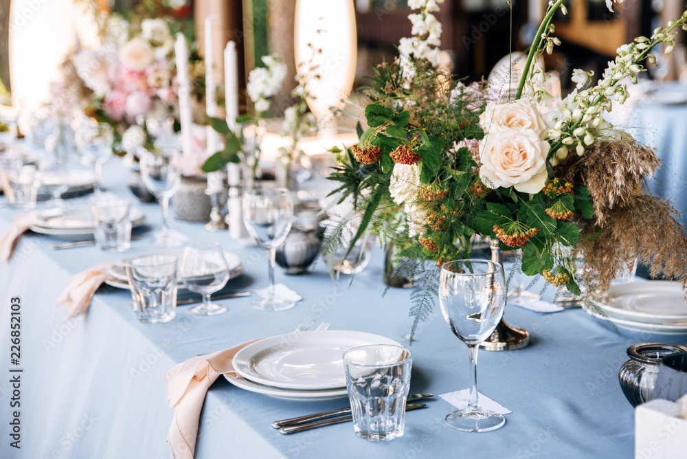 Festive table decorated with flowers and candles on a silver candlestick on blue tablecloth