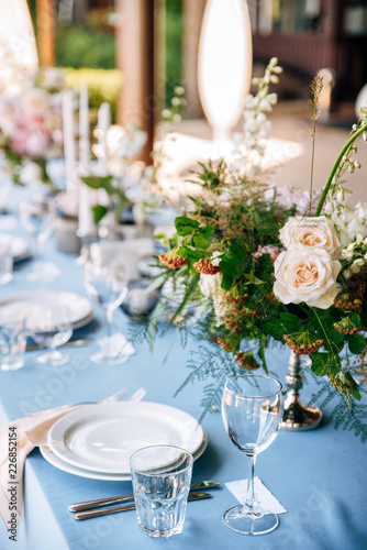 Festive table decorated with flowers and candles on a silver candlestick on blue tablecloth