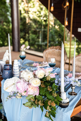 Festive table decorated with lond tablecloth and white flowers with greens under garland in rustic style photo