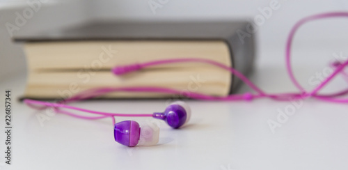 Headphones sticking out of a book on a light background, the theme of an audiobook