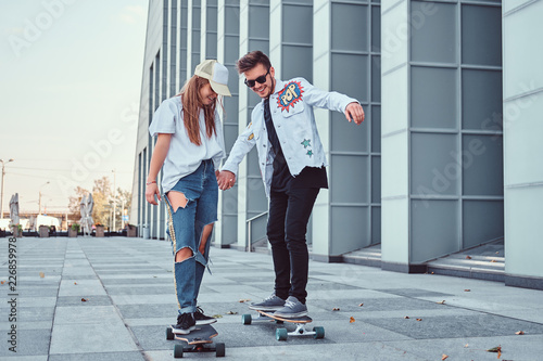 Foto Happy young couple having fun while driving skateboards on a modern street