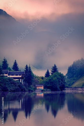 Foggy morning on a lake in the mountains with some houses on the shore