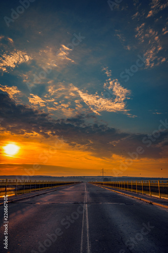 Road bridge over a river at sunrise against a blue sky with clouds