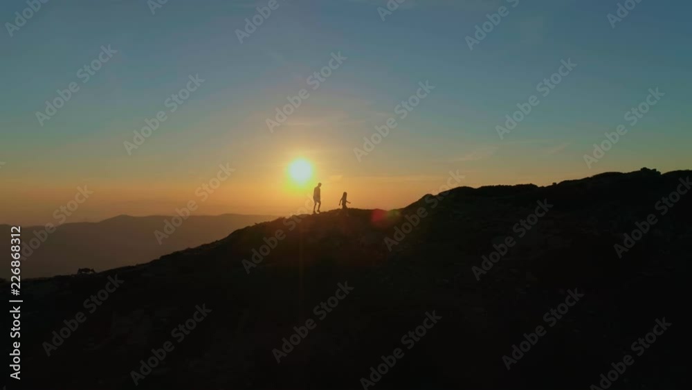 Amazing and inspiring romantic sunset over high mountains. Two people hike and camp, walk on crest edge of mountain peak, reaching goal or finish line. Motivational moment for achievements