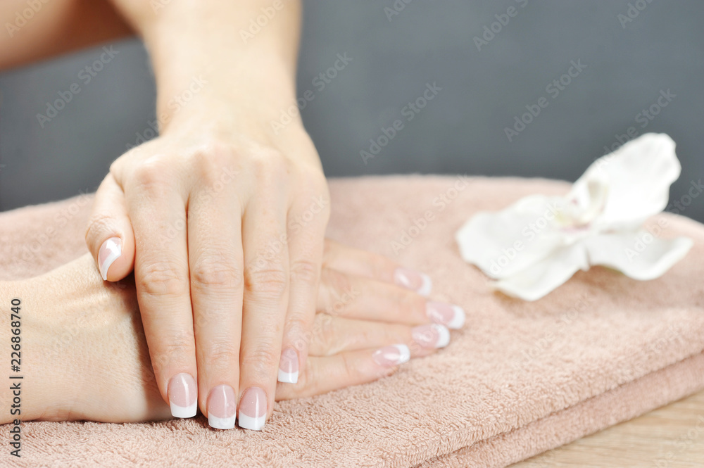 French manicure. In the frame, two women's hands rest on a towel. Near the white orchid flower. Close-up. 