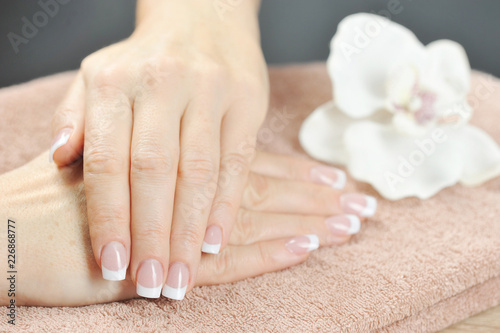 French manicure. In the frame  two women s hands rest on a towel. Near the white orchid flower. Close-up. Macro shooting.