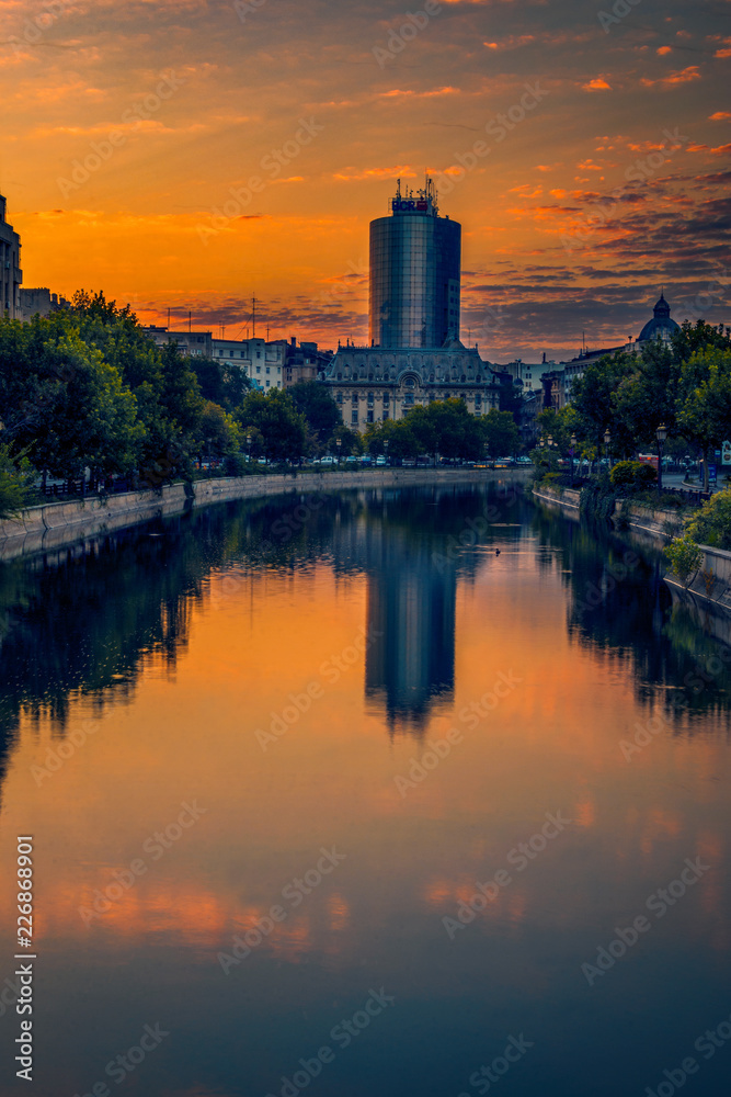 Scene from the Bucharest city in Romania early in the morning with a big glass building skyscraper in the background and a river with some ducks swimming