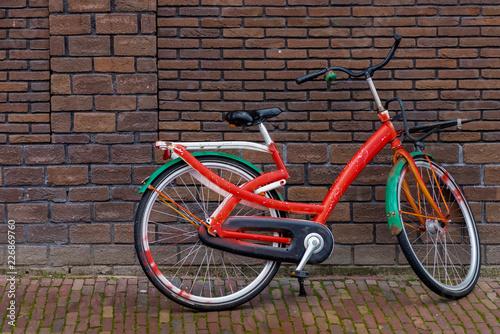 Bicycle painted in white, red and green, leaning against a brick wall