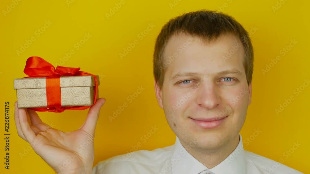 guy with gift inside the box smiles and looks into the camera, on yellow wall background guy with gift inside the box smiles and looks into the camera, on yellow wall background