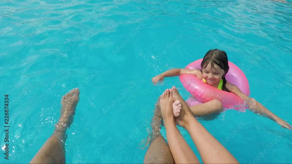 The child swims in the pool next to the parents. The legs of a married couple in the pool. The child swims in the pool next to the parents. The legs of a married couple in the pool.