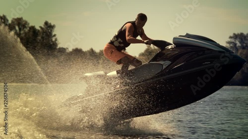 Active man riding jet ski at sunny day. Rider jumping on jet ski on waves. Sportsman having fun on jetbike in slow motion photo