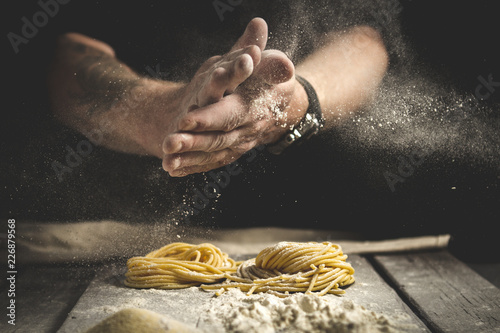 A man claps his hands and sprinkles flour on fresh pasta. Black background, rustic style