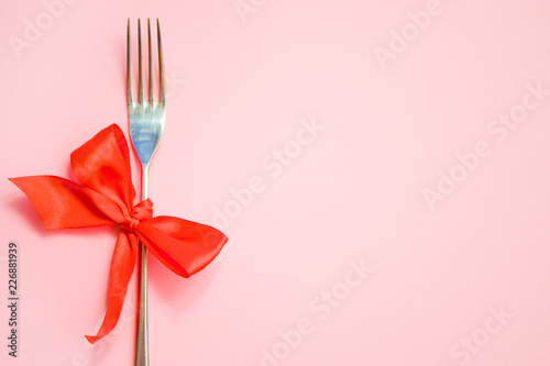Top view of metal fork with red bow on pink background. space for text. Christmas, New Year, Birthday food, holidays, celebration concept