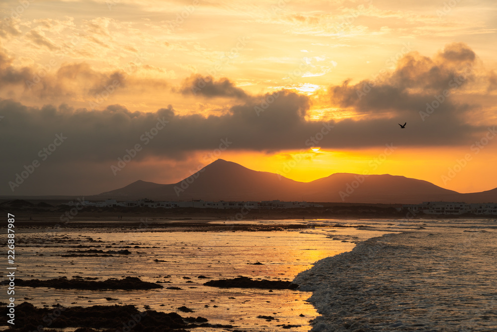 Yellow sunset with the sun in the frame over the mountains reflected in the wet sand of the ocean coast