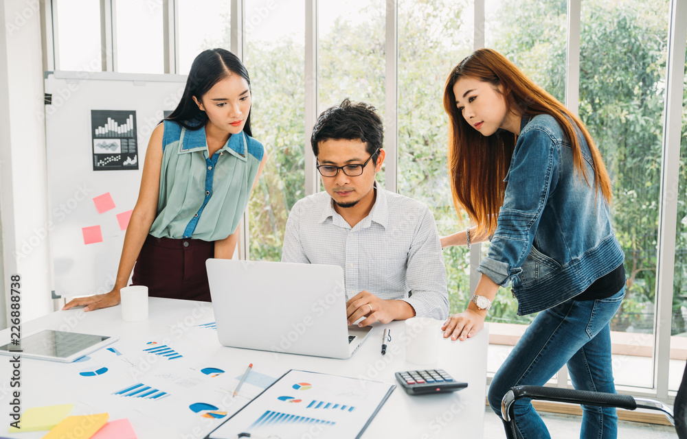 Young asian casual businessman and woman meeting in modern office. Teamwork concept. Business partner presenting working information on laptop with analysis graph documents on table Young asian casual businessman and woman meeting in modern office. Teamwork concept. Business partner presenting working information on laptop with analysis graph documents on table