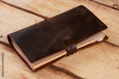 Old vintage leather book on wooden background. Handmade paper diary notebook in brown leather cover