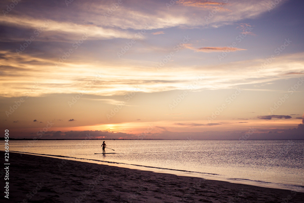 silhouette woman paddle boarding at sunset in bay