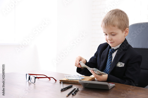 Cute little boy counting money at table indoors