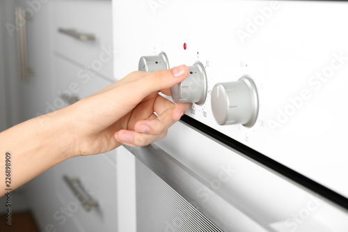 Woman adjusting electric oven in kitchen, closeup