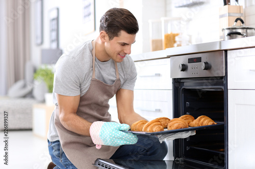 Man taking baking tray with delicious croissants out of electric oven in kitchen