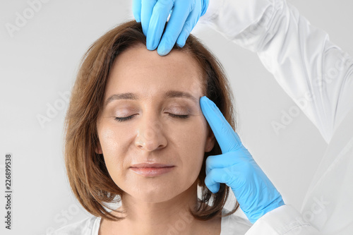 Doctor examining mature woman face before cosmetic surgery on white background