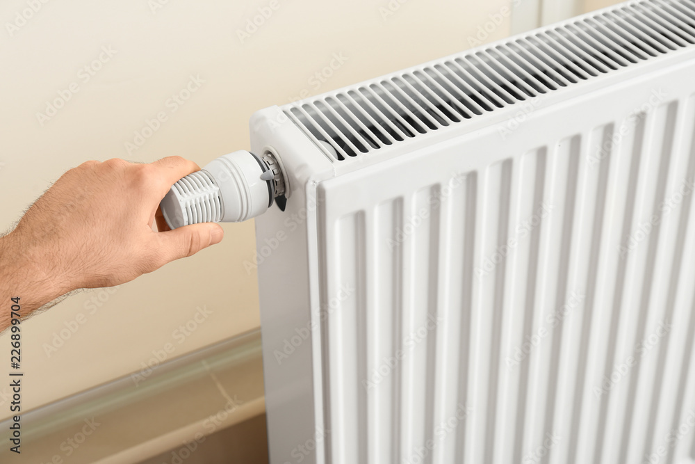 Man adjusting heating radiator thermostat indoors Man adjusting heating radiator thermostat indoors