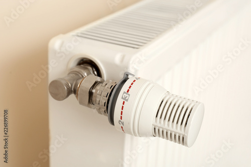 Heating radiator with thermostat near light wall indoors