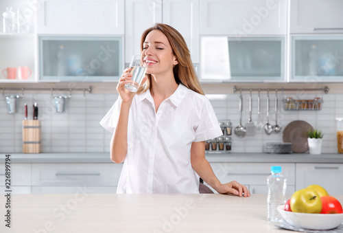Young woman drinking clean water from glass in kitchen