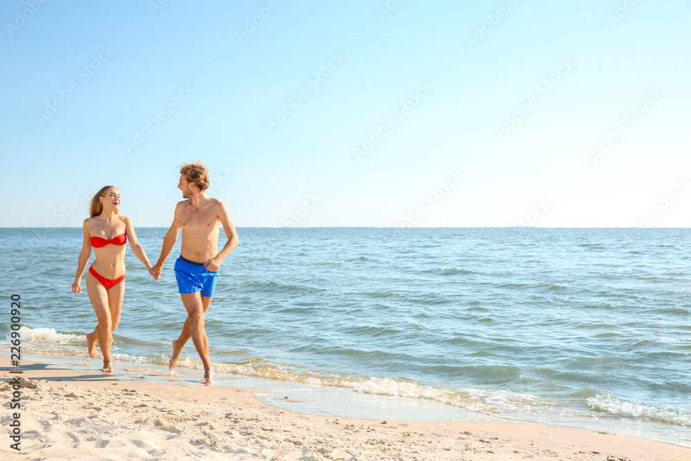 Happy young couple in beachwear walking together on seashore