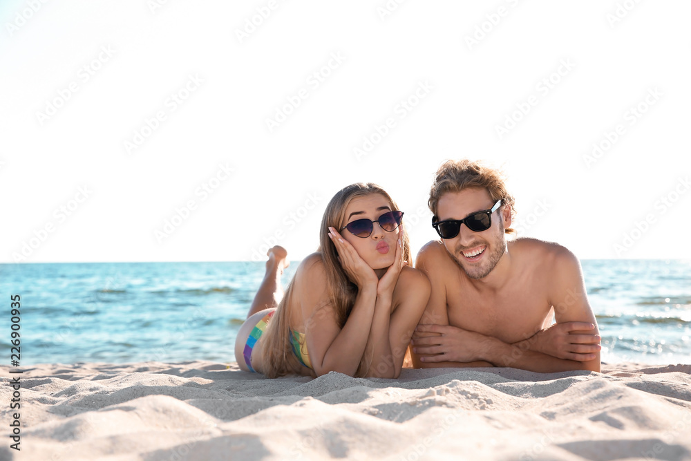 Happy young couple in sunglasses lying together on beach Happy young couple in sunglasses lying together on beach