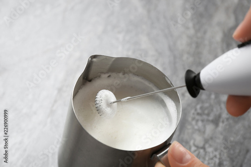 Woman using milk frother in pitcher on table, closeup photo