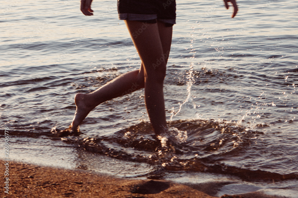 Girl's legs in shorts walking along the beach