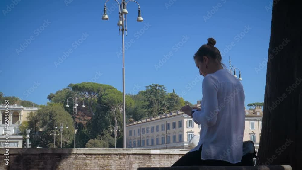 girl uses a smartphone on Piata di Popolo in sunny Rome girl uses a smartphone on Piata di Popolo in sunny Rome