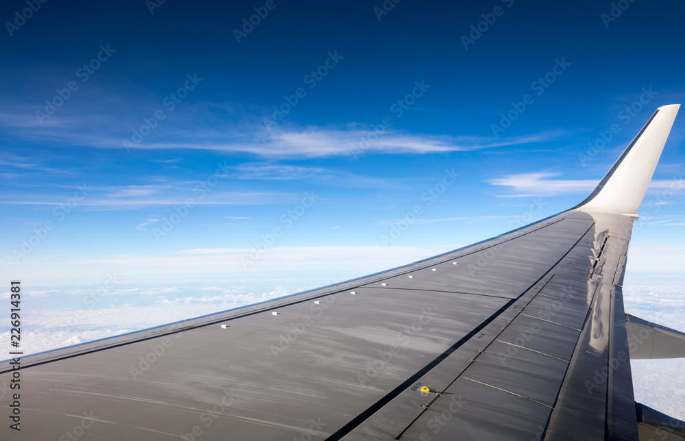 Wing of the plane on blue sky background. View of plane wing and sky from airplane window. Wing airplane over blue sky