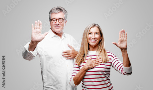 Принти на полотні senior cool husband and wife smiling confidently while making a sincere promise or oath, solemnly swearing with one hand over heart