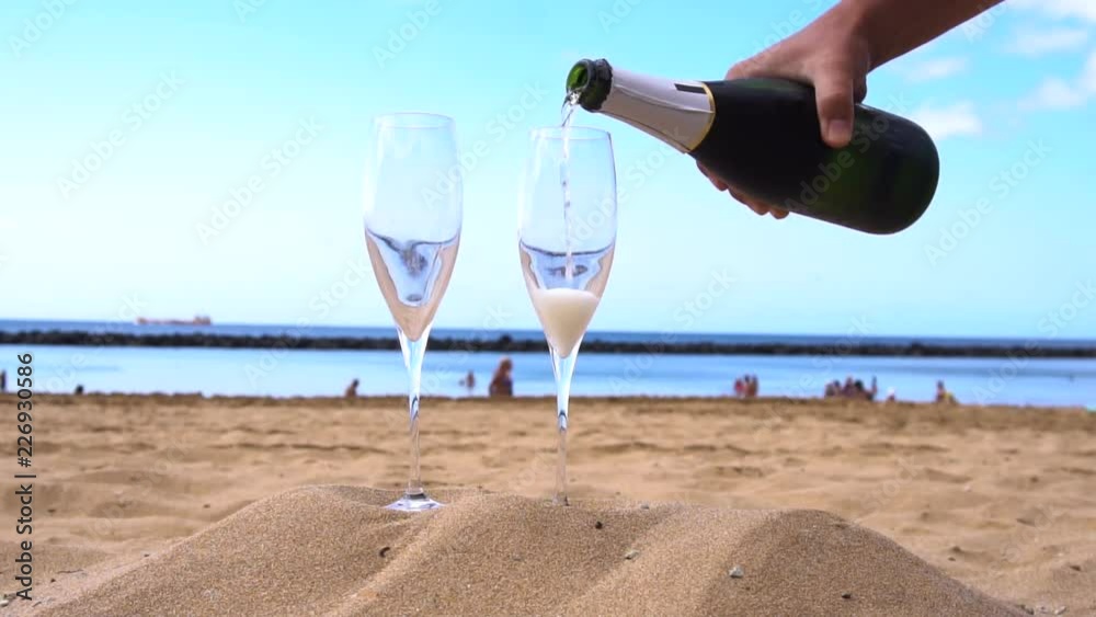 champagne on beach - someones hands pouring drink into the glasses, slow motion champagne on beach - someones hands pouring drink into the glasses, slow motion