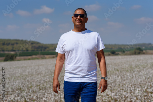 Portrait Of Handsome Active Senior Man Outdoors. Sporty athletic elderly man on background of sky and cotton field. Senior farmer standing in meadow background.