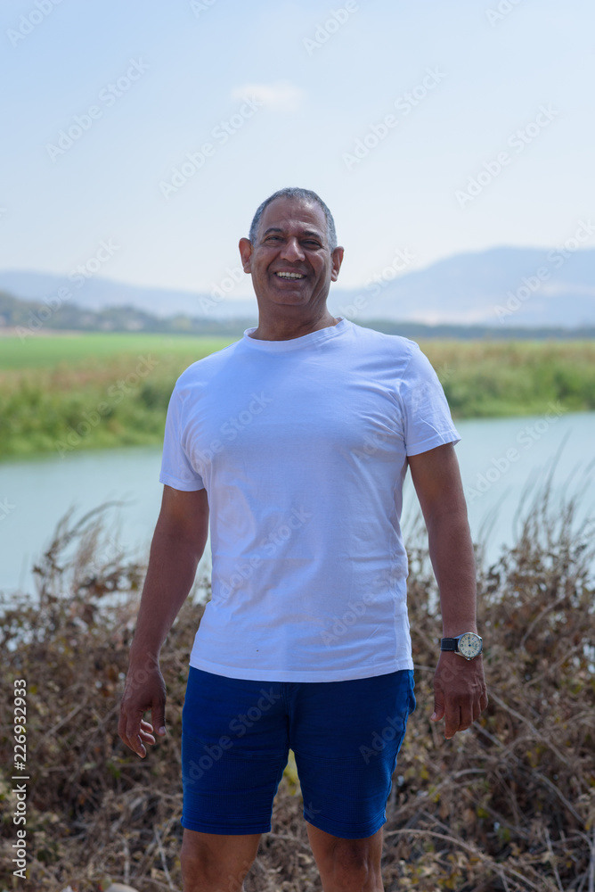 Portrait Of Handsome Active Senior Man Outdoors. Sporty athletic elderly man on background of sky and cotton field. Senior farmer standing in meadow background.