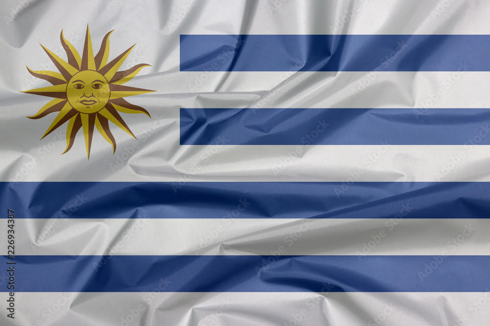 Fabric flag of Uruguay. Crease of Uruguayan flag background, horizontal of white alternate with light blue and the Sun of May. Stock Photo | Adobe Stock