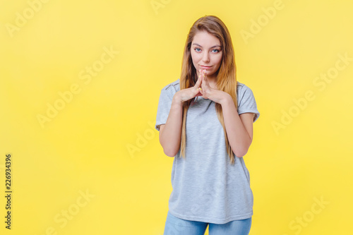 Tableau sur toile Girl on a yellow background looks with a smile with folded hands in face