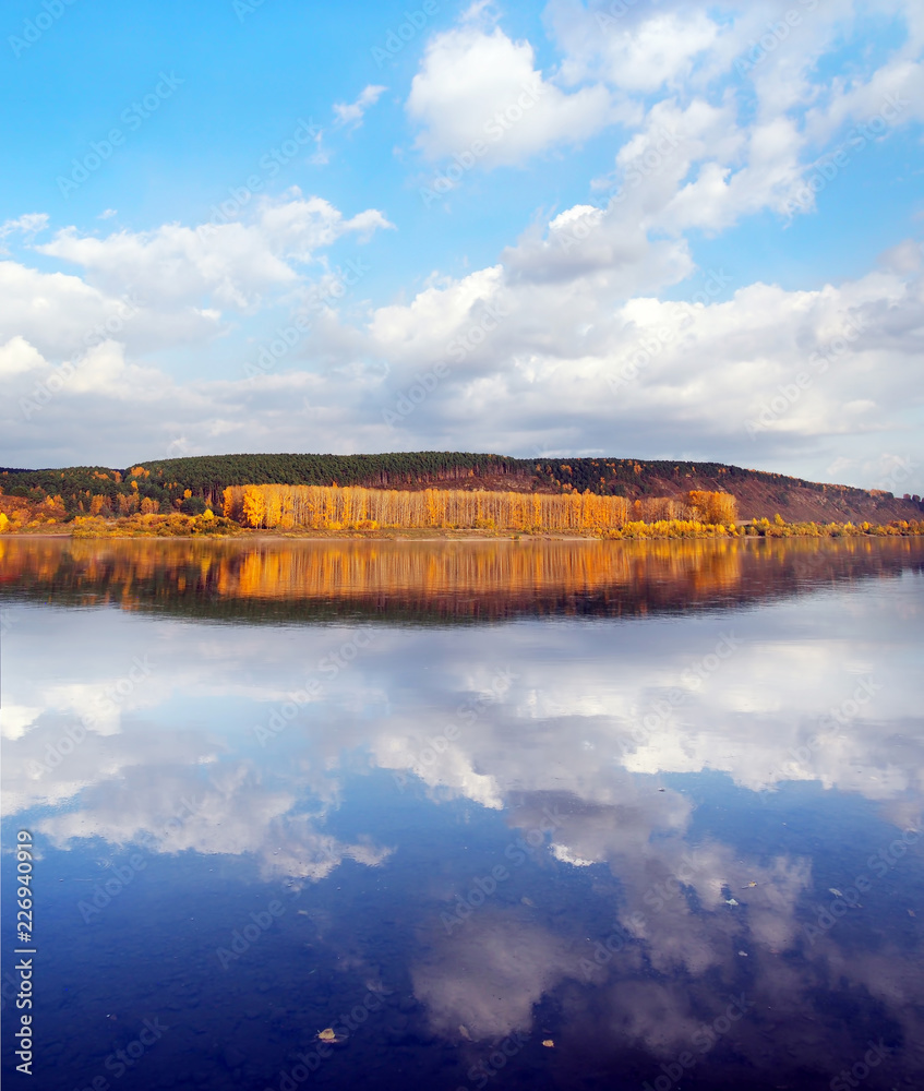 Beautiful autumn landscape with reflections of clouds in water and bright yellow river bank on sunset