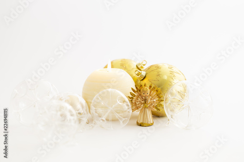 Still life with beautiful decorative transparent and gold colored christmas glass balls, a round satin colored burning candle, a satin star ornament and a straw angel on white background