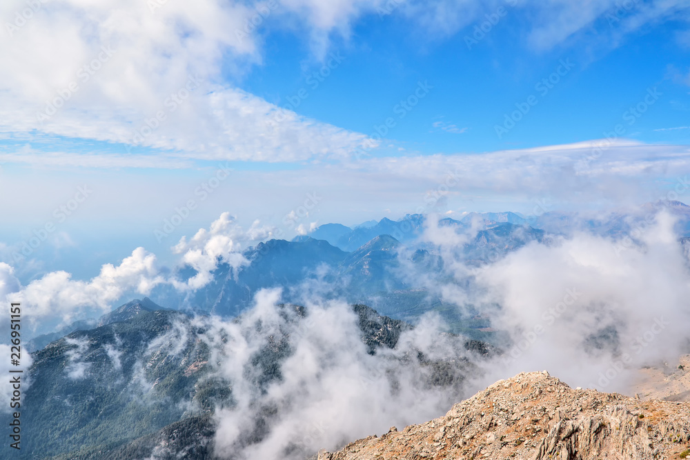 View from the Peak of Tahtali Mountain or Olympus to the tops of the Taurus Mountains, against the background of the cloud and the blue sky
