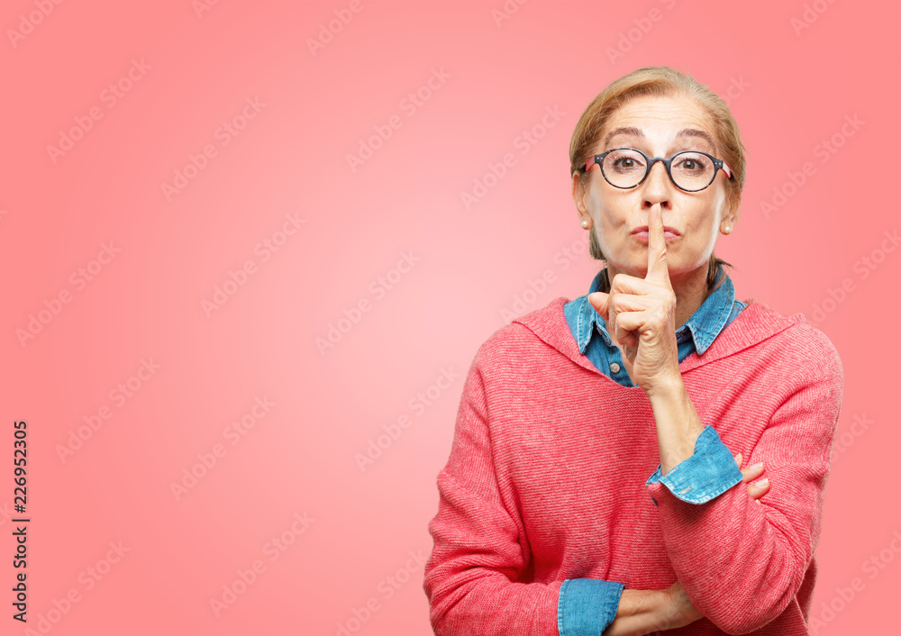 Beautiful senior woman gesturing "keep quiet" with hand, hushing you and demanding silence with a serious, stern look. - obrazy, fototapety, plakaty 