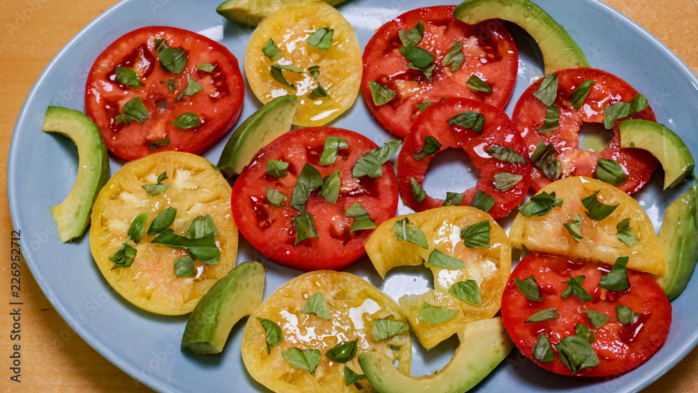 A colorful, simple salad of tomatoes, avocados, basil and olive oil on a blue platter tempts the diner with a fresh, healthy treat A colorful, simple salad of tomatoes, avocados, basil and olive oil on a blue platter tempts the diner with a fresh, healthy treat