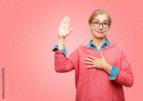 фотографія Beautiful senior woman smiling confidently while making a sincere promise or oath, solemnly swearing with one hand over heart