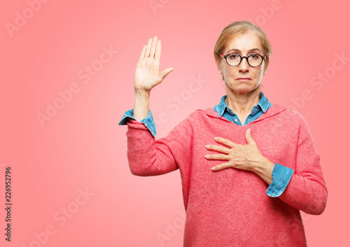 фотографія Beautiful senior woman smiling confidently while making a sincere promise or oath, solemnly swearing with one hand over heart