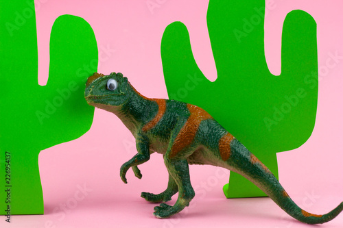funny green dinosaur toy and paper craft cacti on pastel pink background