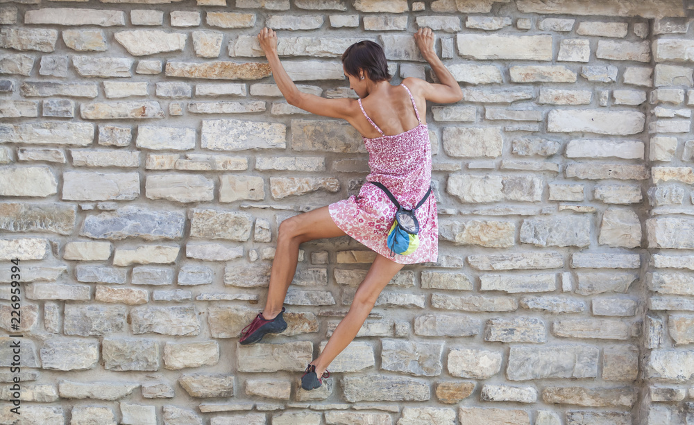The girl climbs the stone wall.