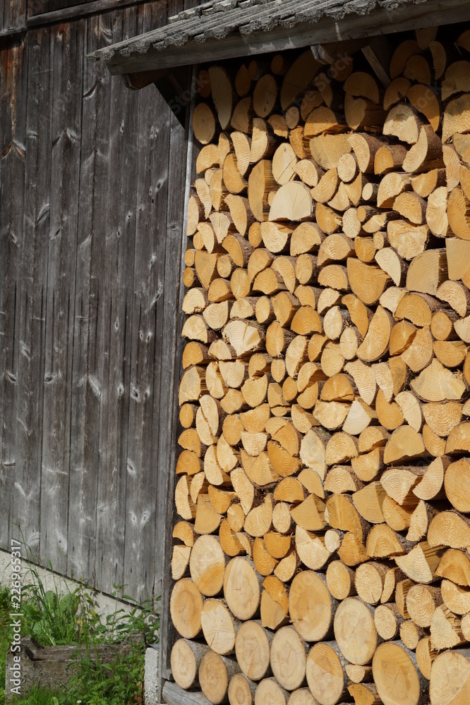 neatly stacked wood with a slightly prominent forward roof, round log at the bottom, up to quarters at the top and a wooden barn wall neatly stacked wood with a slightly prominent forward roof, round log at the bottom, up to quarters at the top and a wooden barn wall